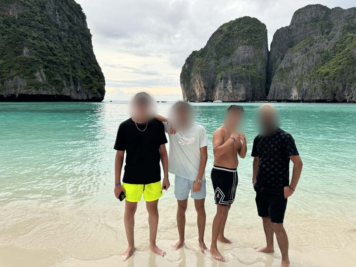Four friends on a tropical beach in daylight, cliffs and turquoise water behind them